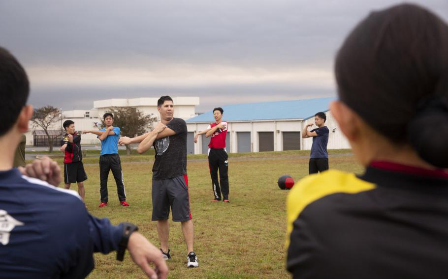 U.S. Marine Sgt. Henry Velasco, electronics maintenance technician with Combined Arms Training Center (CATC), leads cool-down stretches during physical training on CATC Camp Fuji, Gotemba, Japan, Oct. 17, 2019. The JGSDF toured the base to learn operations of U.S. Marines, practice speaking English, and to strengthen the relationship between two nations. (U.S. Marine Corps photo by Cpl. Sarah Stegall)