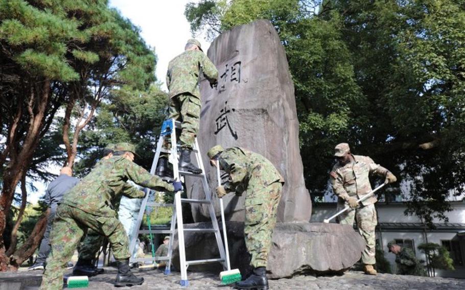 Soldiers assigned to the 765th Transportation (Terminal) Battalion and members of the Japan Ground Self-Defense Force work together to beautify the large “Sobudai” stone monument Nov. 19 on Camp Zama.