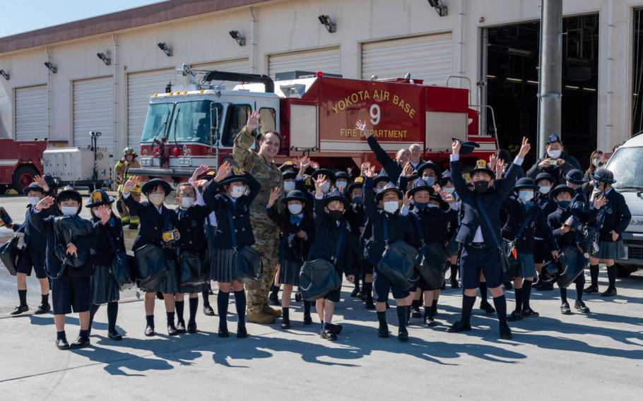 Tech. Sgt. Peter Beyer, the 374th Civil Engineer Squadron Fire Department NCOIC of logistics, and second grade students from Keimei Gakuen Elementary School, located in Akishima, wave for a group photo, Feb. 28, 2023, at the main-base fire station on Yokota Air Base, Japan. The 374th CES Fire Department typically conducts one tour per month as part of the Japanese Local School Partnership Program. (U.S. Air Force photo by Airman 1st Class Natalie Doan)