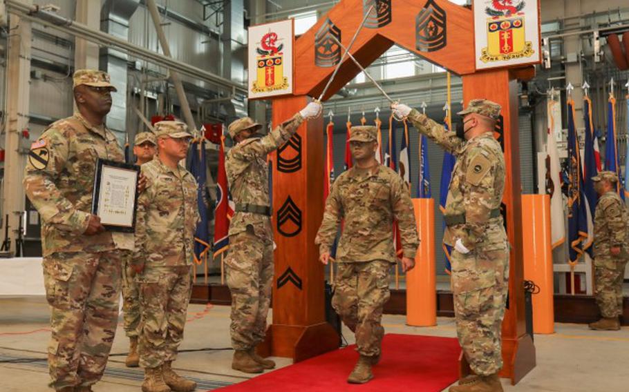 Sgt. Ulises Huang, center right, walks under a wooden arch adorned with all the enlisted ranks and a pair of raised sabers to be officially inducted into the NCO corps during a ceremony at Sagami General Depot, Japan, June 10, 2022. (Photo Credit: Sean Kimmons)