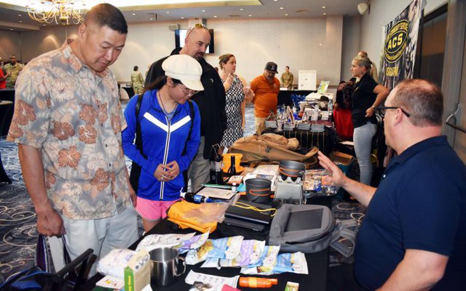 From left, Brian Lim, his daughter Celine Lim and David Carlile look over emergency kits during the emergency preparedness Community Information Exchange at the Camp Zama Community Club May 10. Mike Dahle, right, an occupational safety and health specialist for U.S. Army Garrison Japan, displayed two of his personal kits as examples. (Photo Credit: Wendy Brown, U.S. Army Garrison Japan Public Affairs)