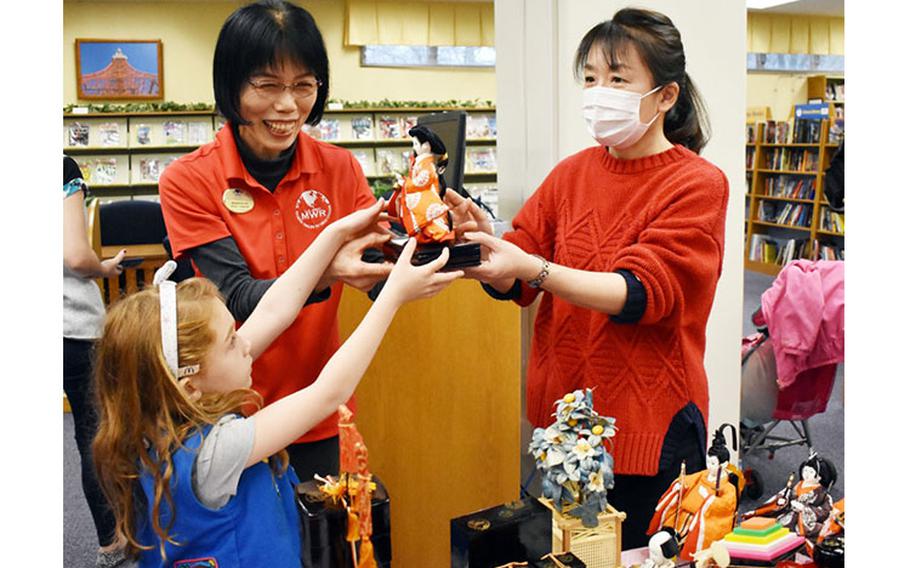 Harumi Kondo, left, and Eiko Kato, staff members at the Camp Zama Library, hand Elizabeth Brown, 6, a member of Daisy Troop 57, a Hinamatsuri doll for display at the Camp Zama Library, Camp Zama, Japan, Feb. 26, 2020.