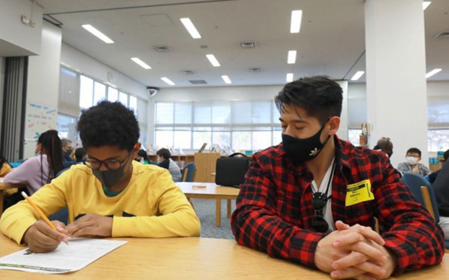 Noah Mills, left, a fourth-grader at Arnn Elementary School on Sagamihara Family Housing Area, Japan, writes down answers from William Birdsall, right, Nov. 10 at the school’s library. Birdsall, an Army veteran who now works as a program assistant at the Camp Zama Youth Center, was there with five other military veterans to be interviewed as part of a Veterans Day project for teacher Jami LeFebre’s class. (Photo Credit: Dustin Perry, U.S. Army Garrison Japan Public Affairs)