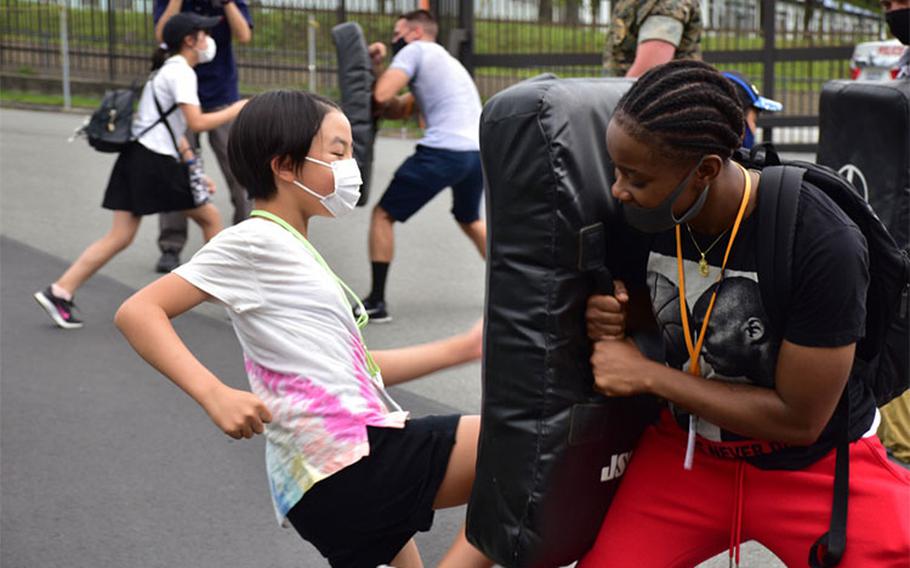 A local Japanese child practices kicking a training pad held by Sgt. Takiyah Wesley, Combined Arms Training Center Camp Fuji supply sergeant, Aug. 7, 2021, Shizuoka, Japan. Marines and Sailors from the installation volunteered at the National Chuo Youth Friendship Center’s fifth annual English camp, where they engaged local children in conversation and activities. Wesley is a native of Memphis, Tennessee. (U.S. Marine Corps photo by Katie Gray)