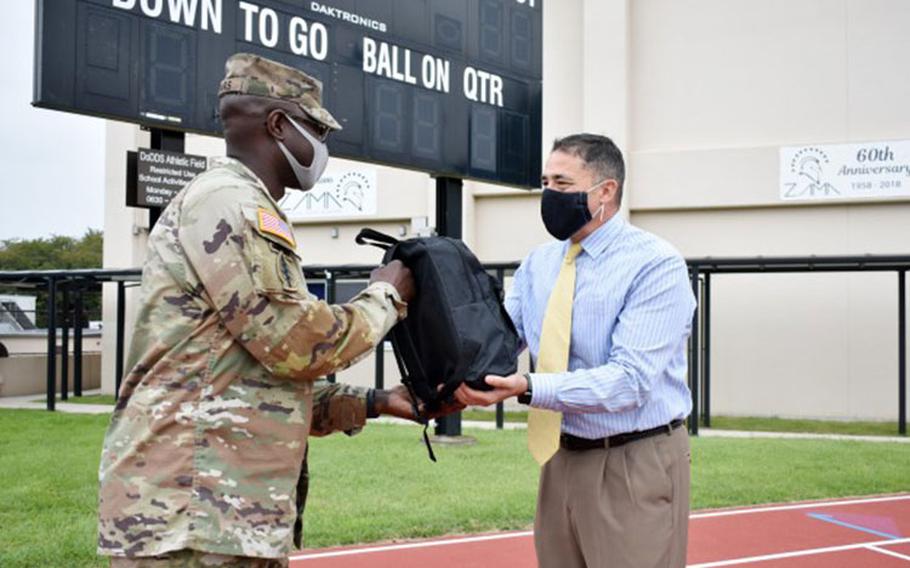 Lt. Col. Demetrick Thomas, left, commander of the 35th Combat Sustainment Support Battalion, hands Henry LeFebre, principal of Zama Middle High School, a backpack full of school supplies at the school, Camp Zama, Japan, Sept. 24. The battalion has an Adopt-A-School Program agreement to sponsor the school. (Photo Credit: Winifred Brown)