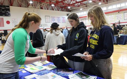 Photo Of A group of Zama Middle High School students receives a sticker from a representative at a booth at the College and Career Fair held March 6 in the ZMHS gymnasium.