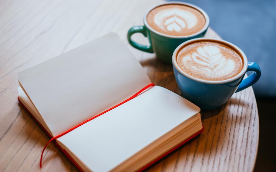 Two blue cups of cappucñino with beautiful latte art and red notebook on the table.