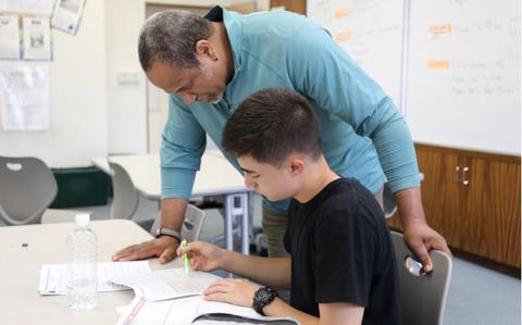 Photo Of A Zama Middle High School student, front, works on an essay while Brian Spivey, rear, an instructional assistant specialist, gives writing tips during a workshop April 27 at ZMHS on Camp Zama, Japan.