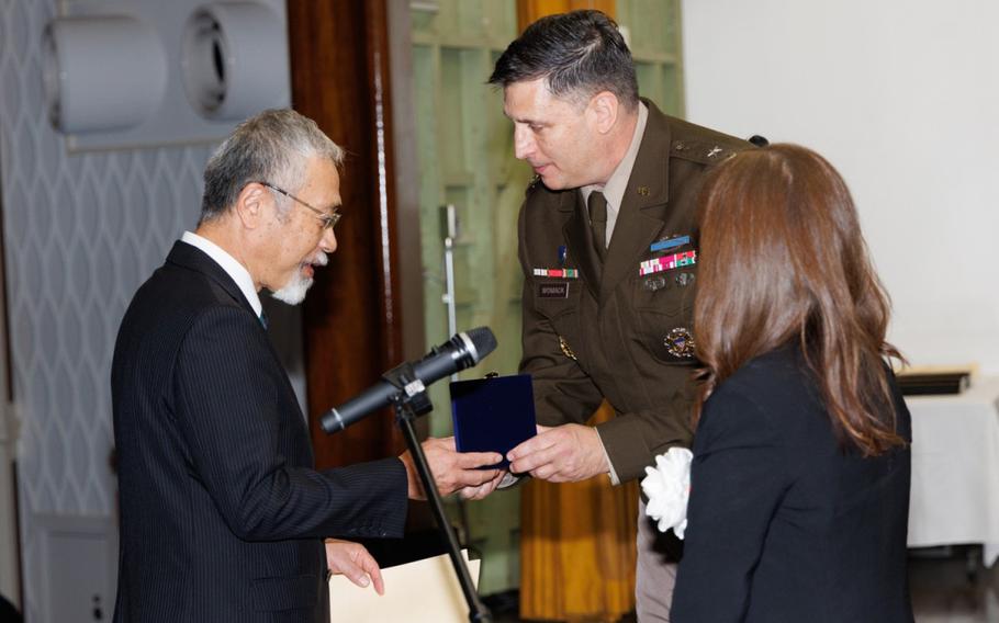 Tsuyoshi Sugahara, an engineer technician for the Directorate of Public Works, receives a commemorative gift from Maj. Gen. Dave Womack on the stage.