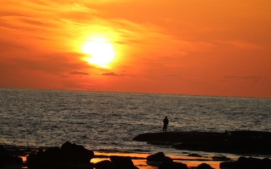 The sunset on the beach. A man is standing on the shore.