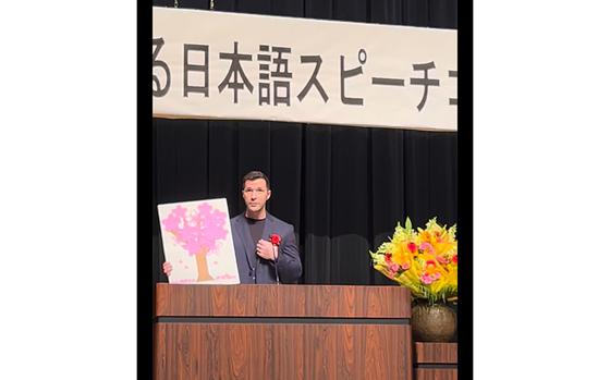 Photo Of Captain Repka gives a speech while holding up a cherry blossom picture made by
Captain Toyota.