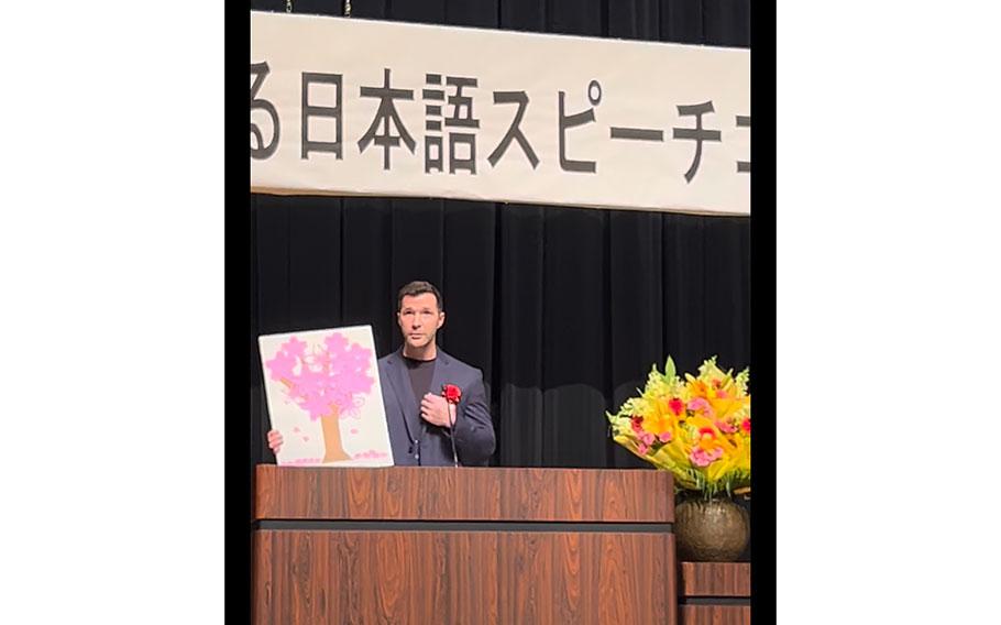 Captain Repka gives a speech while holding up a cherry blossom picture made by Captain Toyota.