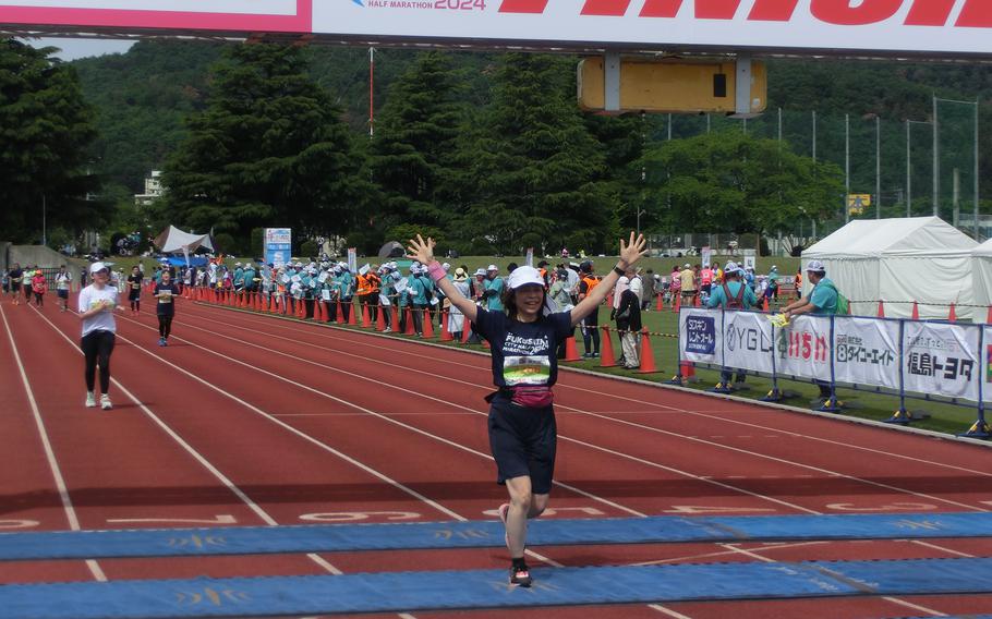 A female participant raising her hands are crossing the finish line.