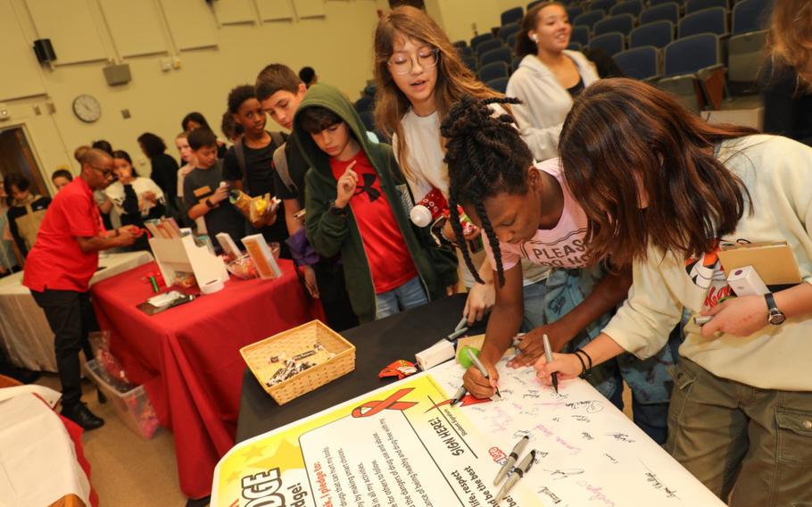 Two of the students are signing and the other students are making a line in order to sign a drug-free pledge.