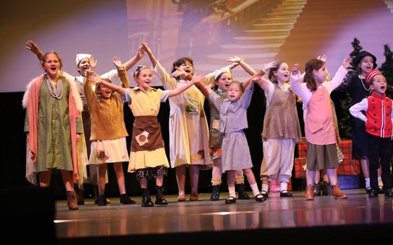 Photo Of Cast members run through a dress rehearsal. Some of them raising both of their hands and singing.