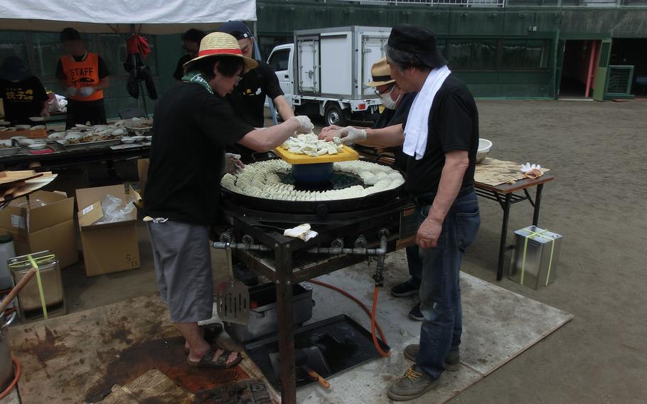 4 people are cooking gyoza with a huge pan for marathon participants.