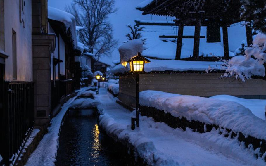 it is snowing in the temple. a small stream can be seen by the temple.