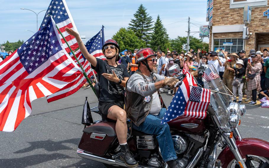 Two men are riding a motorcycle with two American flags.