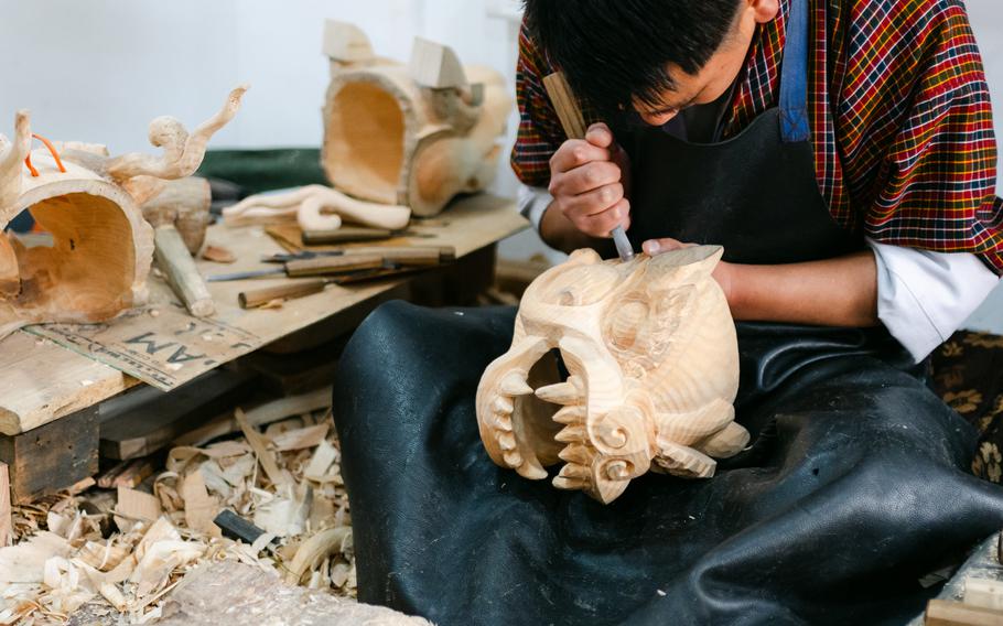 A wood-carving student chisels away at a dragon head.