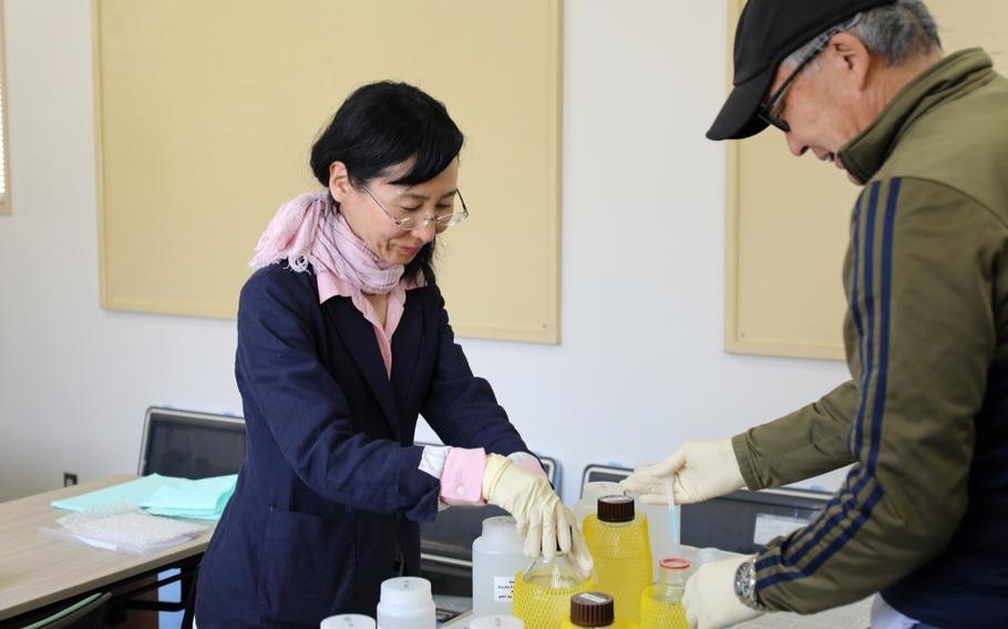 Mikiko checks water samples with a male coworker inside a room.