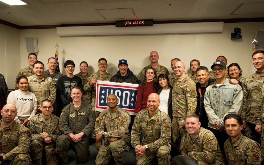 Comedian Jo Koy holding a USO flag poses for a group photo with Yokota Air Base leadership, friends, and family