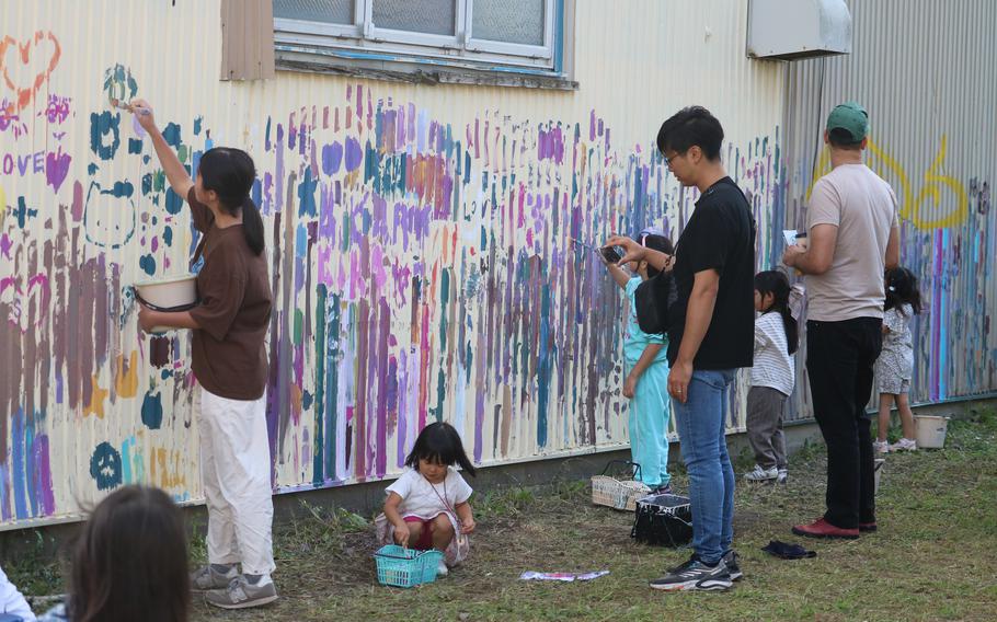 Kids and adults drawing pictures on the wall with paints.