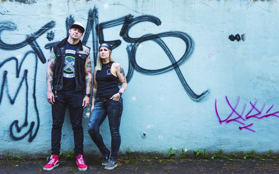 Photo Of two people with tattoos are standing by the wall.