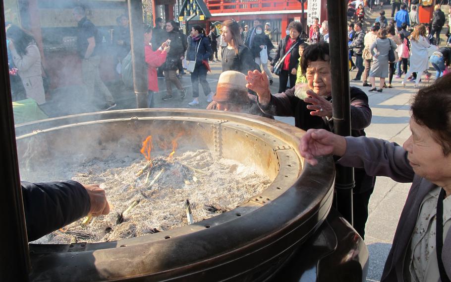 Some elderly people are near a huge incense holder. 