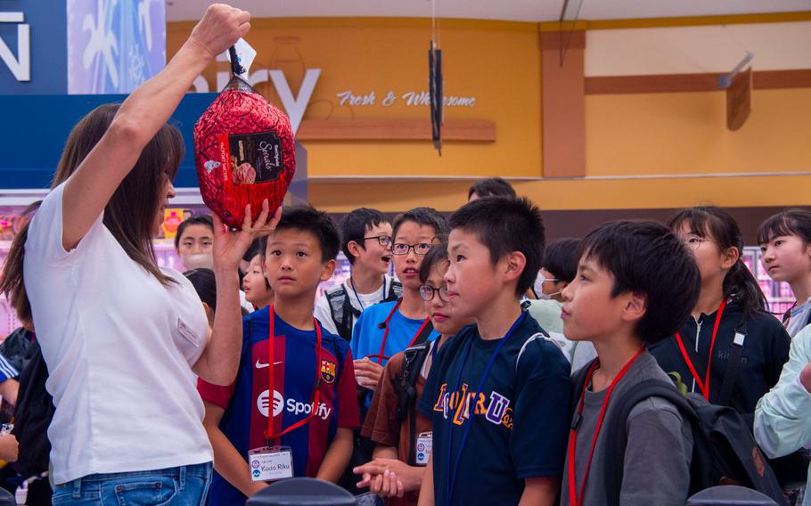 Suntok Crusha, left, Misawa Commissary assistant officer, shows Towada Elementary School students a ham and other food items as they practice their English during a Junior English tour at Misawa Air Base, Japan, July 23, 2024. Junior English tours provide young participants the invaluable opportunity to practice their English language skills in real-world settings, enhancing their confidence and proficiency.