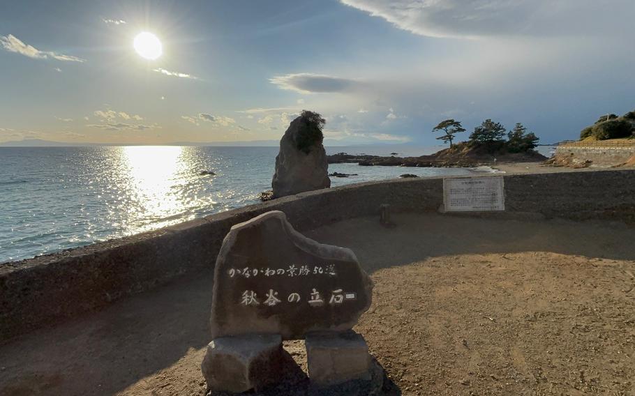 a stone monument in the park and the ocean can be seen from the hill.