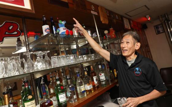 Photo Of Takeshi Kusunoki, a bartender at the Kure Harbor Club, points to plaques that military units have presented to the club for its support at Kure Pier 6, Japan, Sept. 5, 2024.