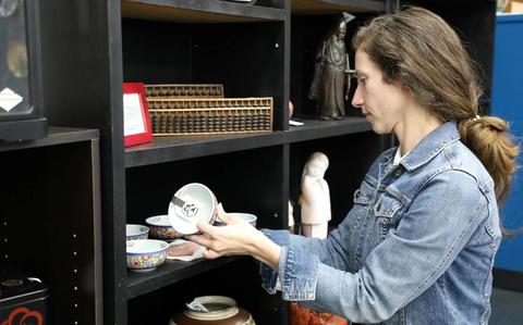 Photo Of Angela Heck, president of the Zama Community Spouses’ Association, cleans a shelf April 17 at the East Meets West Gift Shop on Camp Zama.