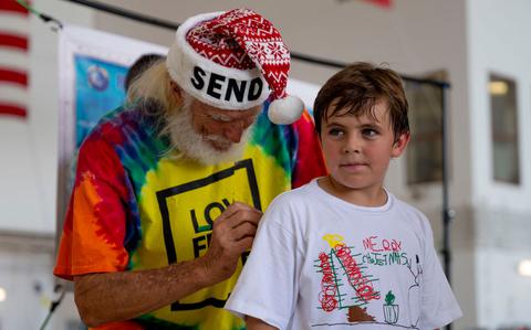 Photo Of Bruce Best, University of Guam researcher, writes a message on a child’s T-shirt during Operation Christmas Drop 2024 at Andersen Air Force Base, Guam, Dec. 7, 2024.