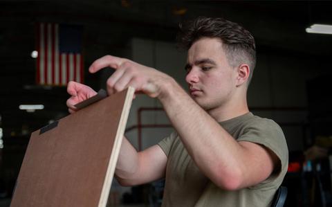 Photo Of U.S. Air Force Airman 1st Class Aleksandr Lepekhin, a combat mobility flight technician with the 374th Logistics Readiness Squadron at Yokota Air Base, Japan, tapes together sheets of wood as part of the bundle building process for Operation Christmas Drop 2024.