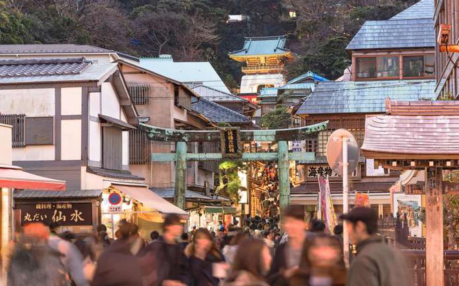 Kanagawa, Enoshima – Dec 25, 2022: Tourists head towards the bronze torii gate of the Enoshima Shrine, leading to the Zuishinmon gate at the top end of the Benten Nakamise Shopping street